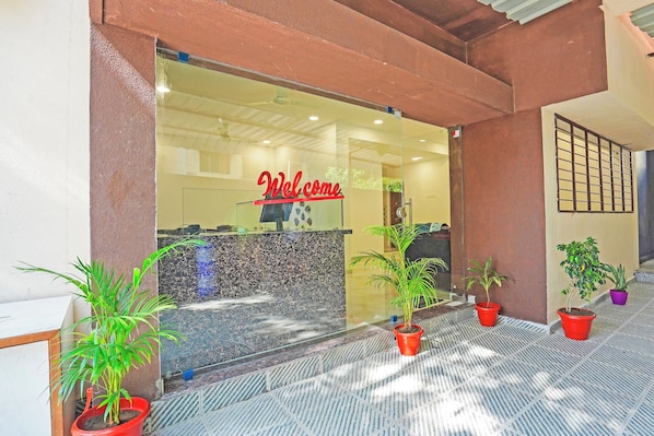 Zona de recepción con un cartel de 'Welcome', mostrador de recepción y plantas en macetas.