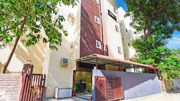 Un edificio con entrada protegida por una reja, un espacio al aire libre techado y una unidad de aire acondicionado a la vista.