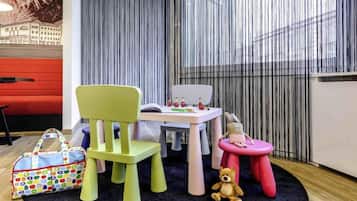 Un espace de jeux pour enfants avec un canapé rouge, une chaise verte, une petite table avec des jouets et un tabouret rose.