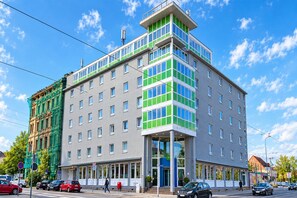 A multi-story hotel with a modern design, featuring a prominent corner entrance and a mix of window styles. - Sunday Hotel Halle Zentrum - Standard Twin Room (Halle (Saale))