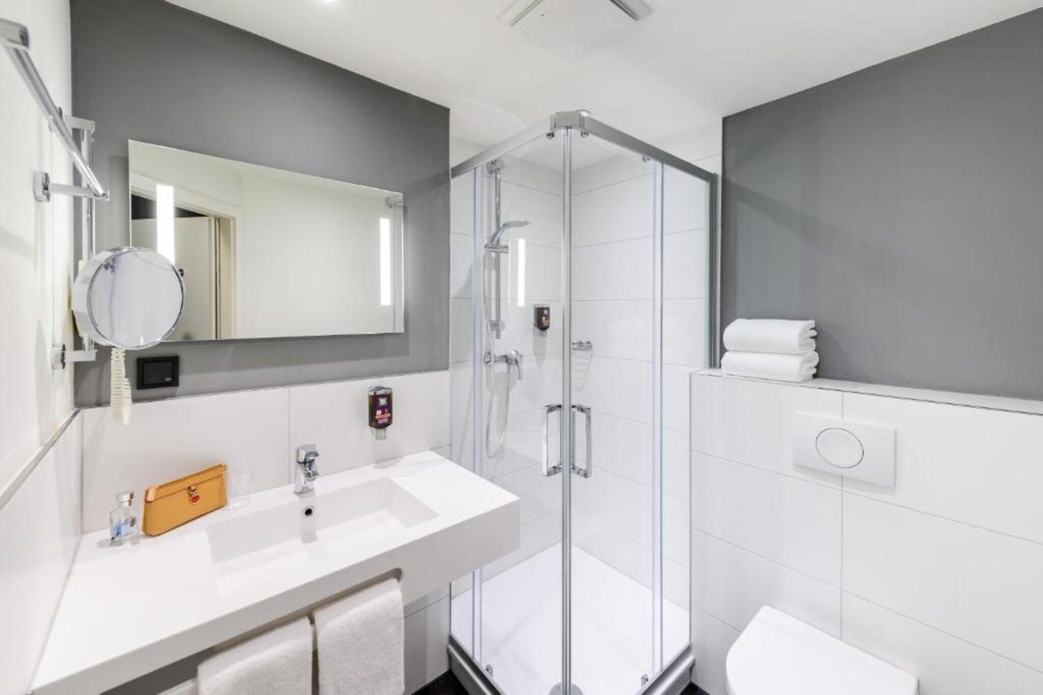 Une salle de bain moderne avec une douche à parois de verre, un lavabo blanc et un grand miroir.