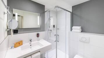 Une salle de bain moderne avec une douche à parois de verre, un lavabo blanc et un grand miroir.
