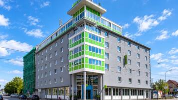 Ein mehrstöckiges Hotel mit modernem Design, das durch eine auffällige grüne und weiße Fassade, große Fenster und einen Eingang im Erdgeschoss gekennzeichnet ist.