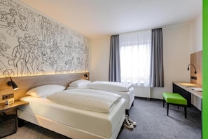 Ein Hotelzimmer mit zwei Betten, einem Schreibtisch, einem Stuhl, einer großen Wandmalerei und einem Fenster mit Vorhängen.