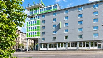 Ein modernes Hotel mit mehreren Etagen, großen Fenstern und einer markanten Fassade in Grün und Grau.