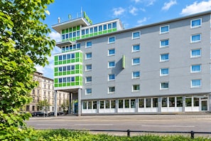 Ein modernes Hotel mit mehreren Etagen, großen Fenstern und einer markanten Fassade in Grün und Grau.