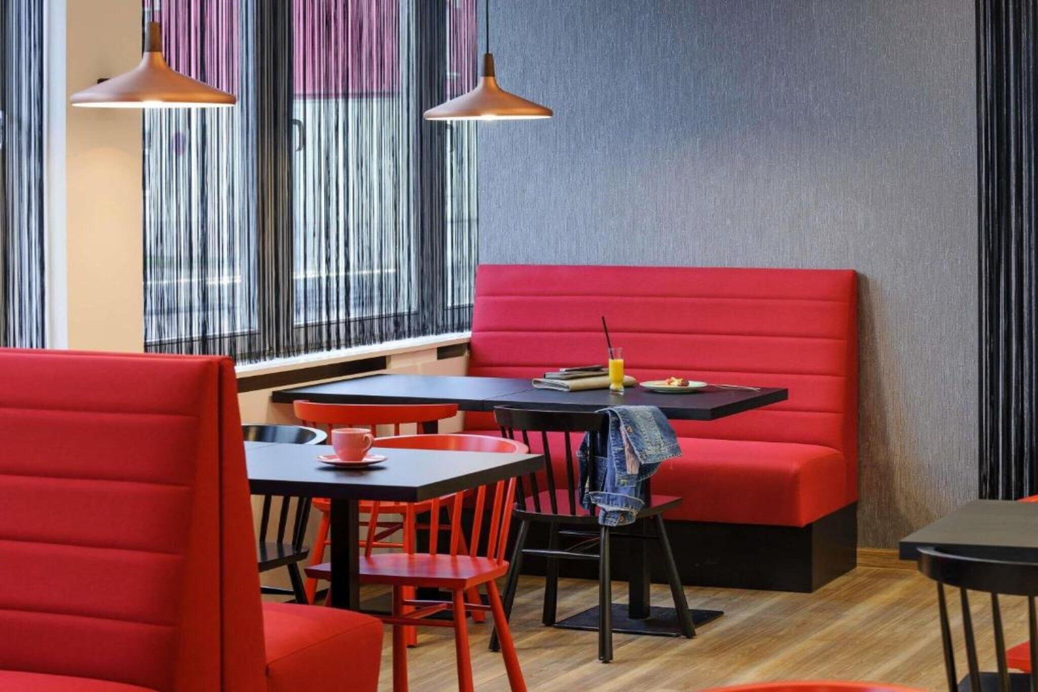 A modern restaurant interior with red seating, black tables, and pendant lighting.