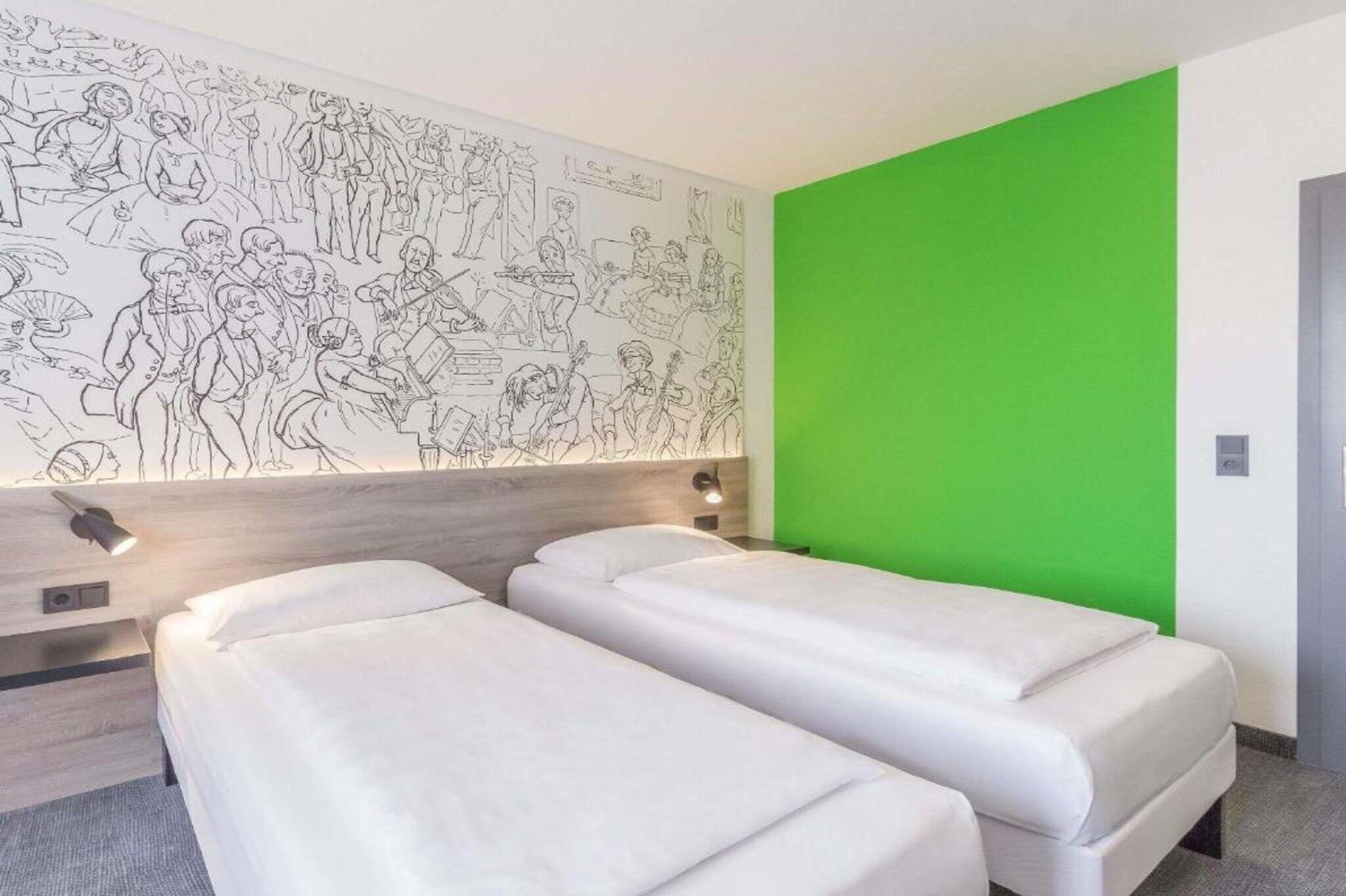 Een hotelkamer met twee eenpersoonsbedden, een groot muurschilderij en een groene accentmuur.