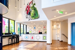 Eine Hotelhalle mit Empfangstresen, gerahmten Kunstwerken an der Wand und einer Treppe.