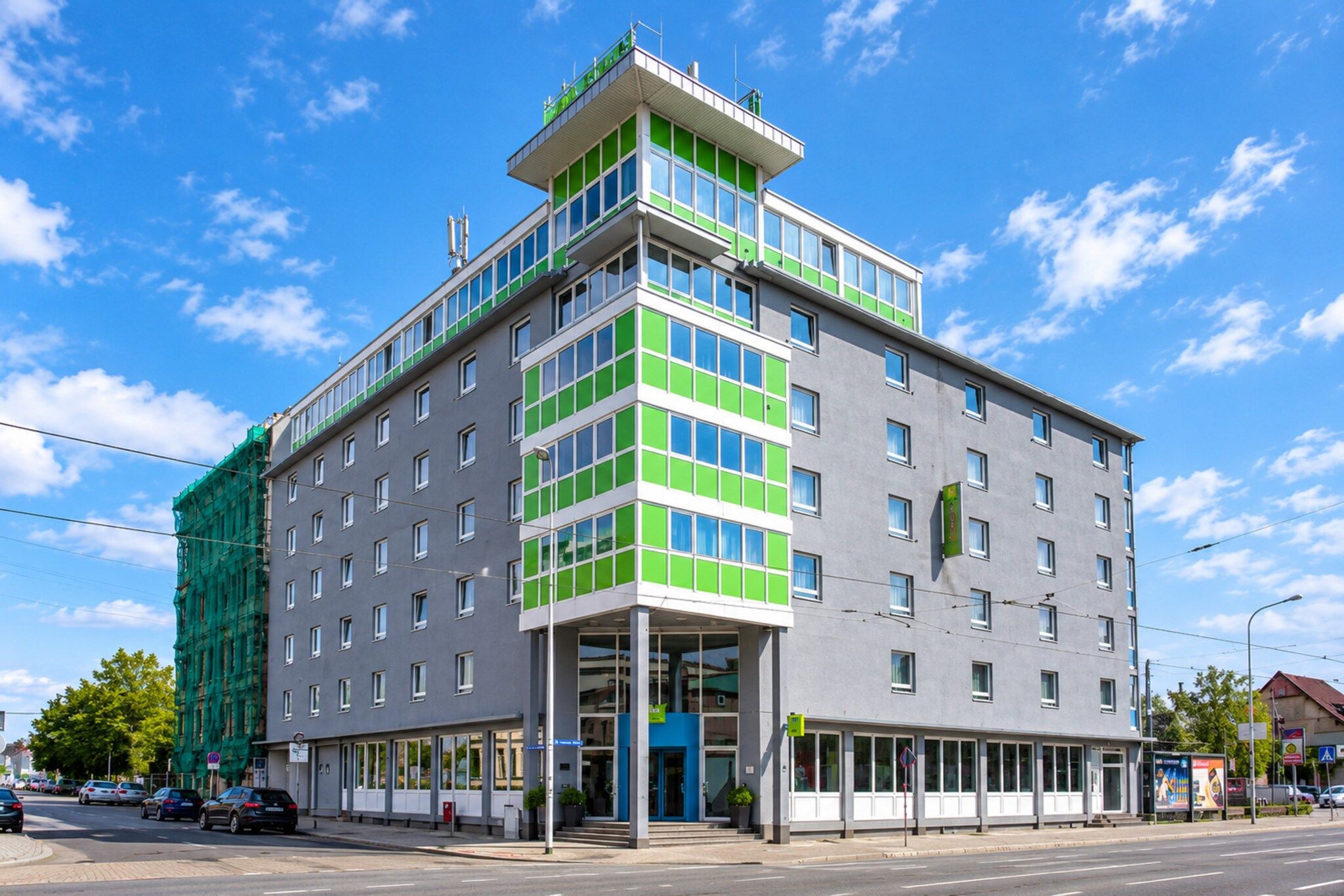 Ein mehrstöckiges Hotel mit modernem Design, das durch eine auffällige grüne und weiße Fassade, große Fenster und einen Eingang im Erdgeschoss gekennzeichnet ist.