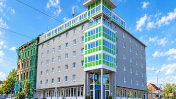 Ein mehrstöckiges Hotel mit modernem Design, das durch einen markanten Eckeingang und unterschiedliche Fensterformen besticht.
