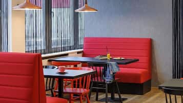 Een modern restaurantinterieur met rode zitplaatsen, zwarte tafels en hanglampen.
