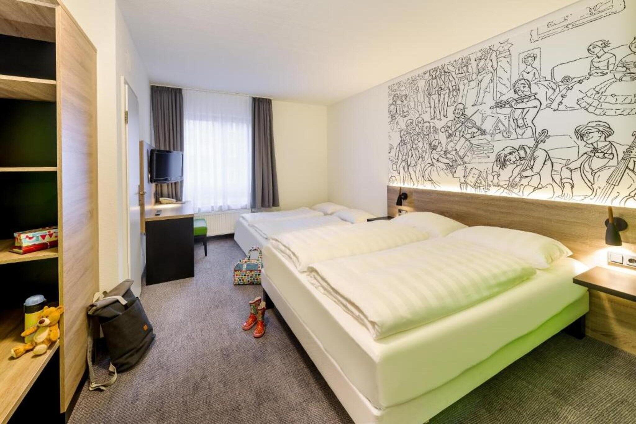 Ein Hotelzimmer mit zwei Betten, einem Schreibtisch, einem Fernseher und einer Wand mit Wandgemälde.