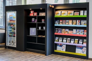 A vending machine and a bookshelf with magazines. - Sunday Hotel Halle Zentrum - Suite (Halle (Saale))