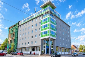 Un hôtel à plusieurs étages au design moderne, caractérisé par une entrée d’angle remarquable et une variété de styles de fenêtres.