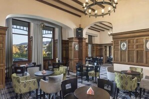 Espaço de refeições de hotel com mesas e cadeiras redondas, painéis de madeira e amplas janelas com vista.