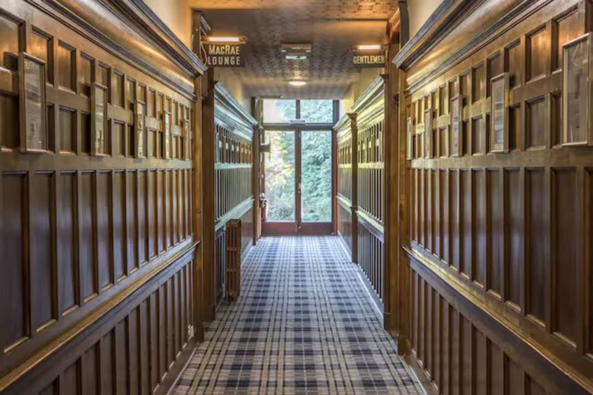 A corridor with wooden paneling and a checkered floor leading to a glass door.
