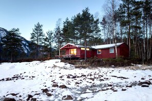 A cabin with a red exterior, surrounded by a forest and snow-covered ground. - Fresh Water Fjord Cabin (Agder)