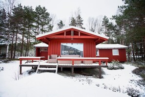 A red cabin with a deck and a large window, surrounded by trees.