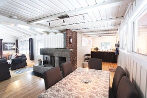 A cozy living room with a fireplace, a dining area with a table, and a kitchen in the background.