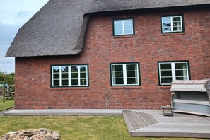 A brick building with a thatched roof, a patio area with a barbecue, and a stone wall. - Holiday home in List with swimming pool (List)