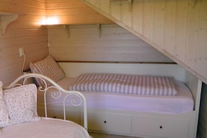 A bedroom with two beds, one with a white metal frame and the other with a wooden frame. There is a small shelf under the bed with a white lamp on it. - Holiday home in List with swimming pool (List)