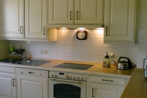 A kitchen with white cabinets, a built-in oven, a sink, and a clock on the wall. - Holiday home in List with swimming pool (List)