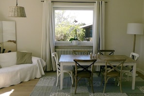 A room with a white sofa, a dining table with chairs, a potted plant on the windowsill, and a lamp on the right. - Holiday home in List with swimming pool (List)