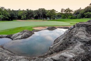 Um campo de golfe com lago, árvores e uma formação rochosa.