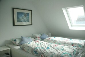 A bedroom with a bed, a nightstand, a framed picture on the wall, and a skylight. - Holiday apartment with 3 bedrooms (Hörnum \/ Sylt)