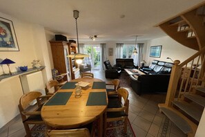 A dining area with a wooden table and chairs, a staircase, and a living room with a sofa and a coffee table. - Holiday home with 4 bedrooms (Carolinensiel)