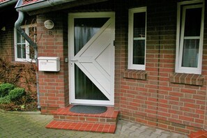 A brick house with a white door and windows, a small porch, and a mailbox. - Holiday home with 4 bedrooms (Carolinensiel)
