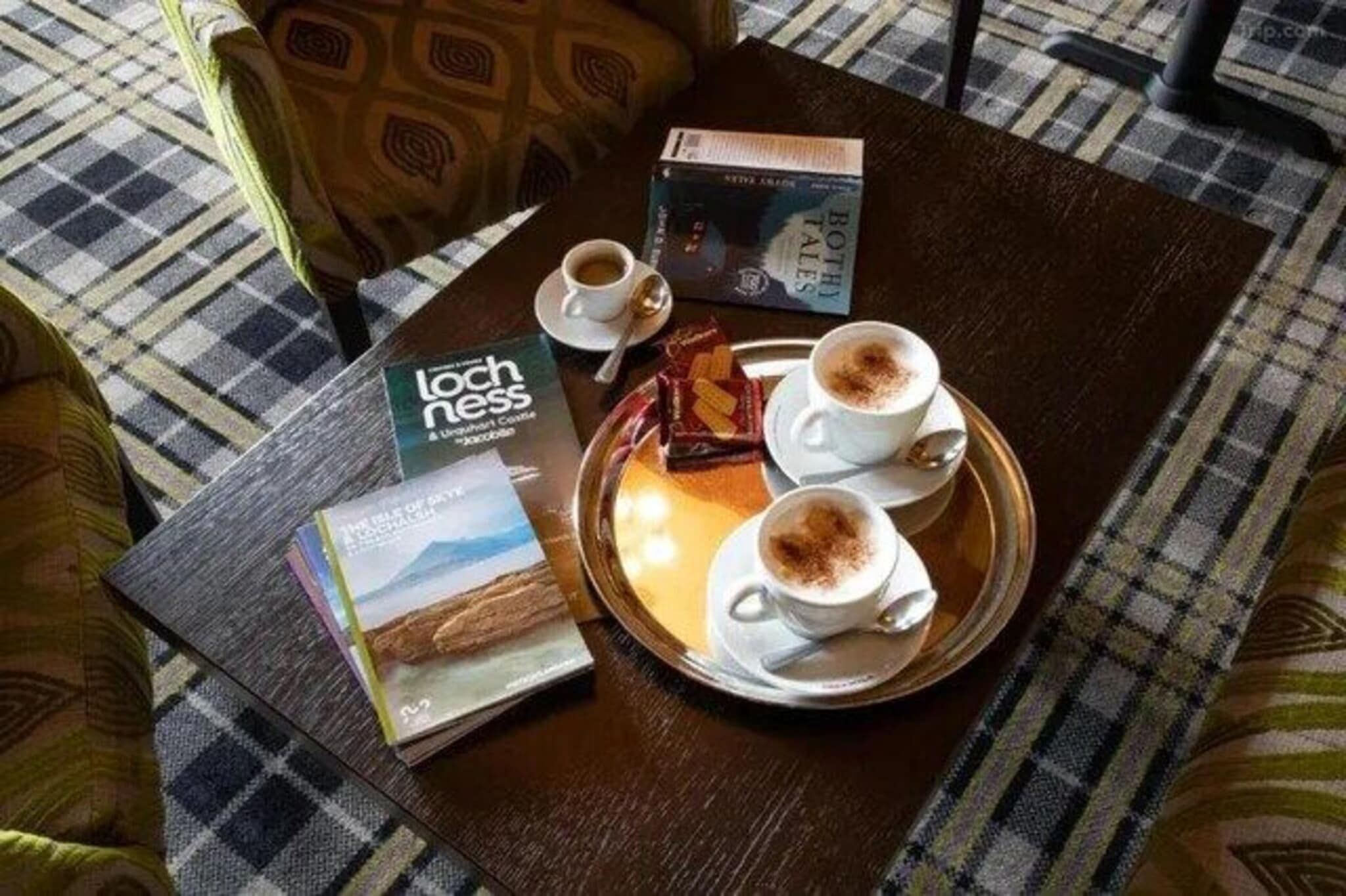 A tray with two cups of coffee and a book titled 'Lochness' on a checkered floor.