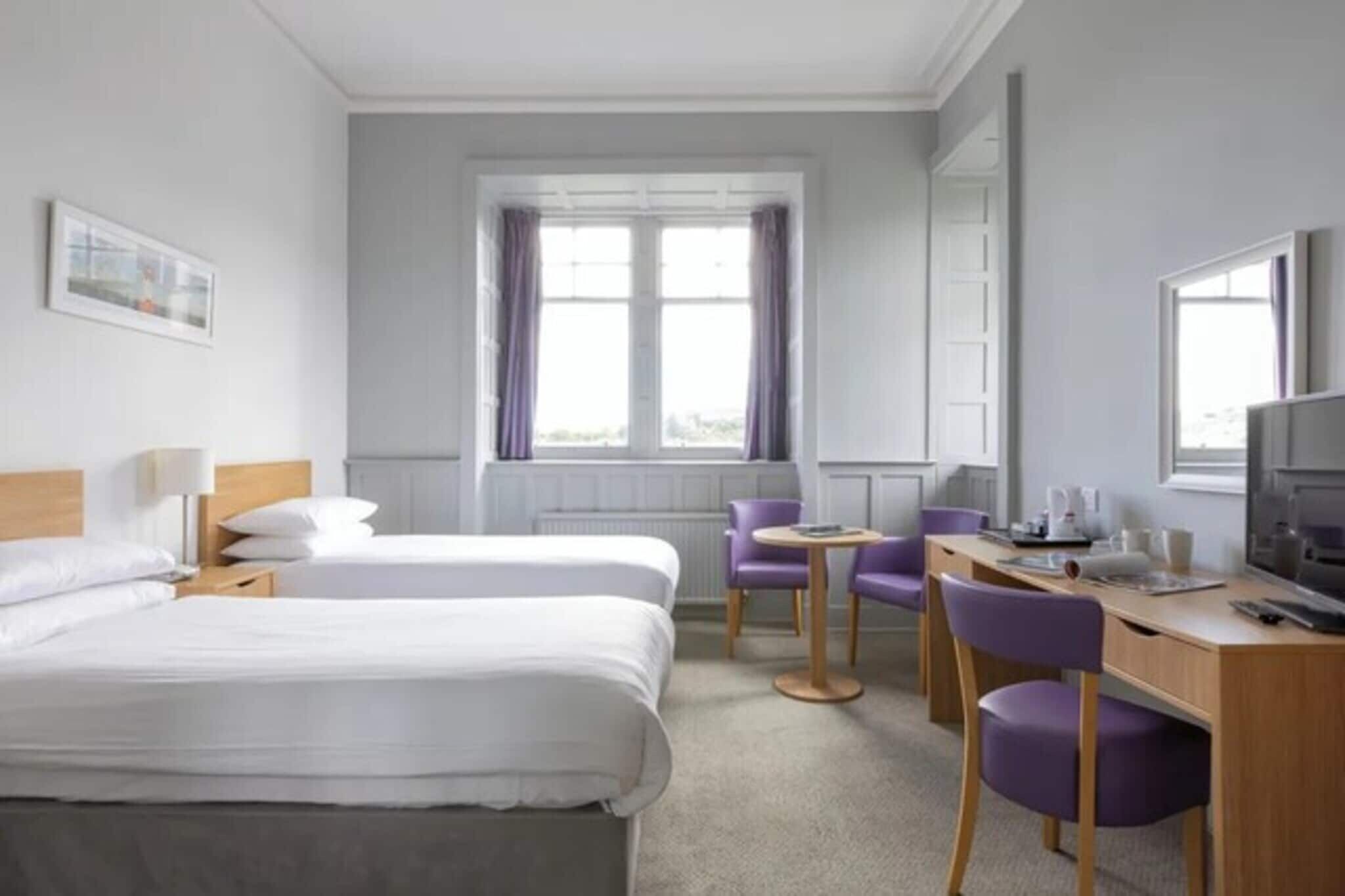 A hotel room with two beds, a desk with a chair, a television, and a window with curtains.