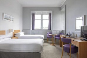 Quarto de hotel com duas camas, uma mesa de trabalho com cadeira, televisão e janela com cortinas.
