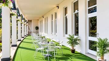 A covered outdoor area with rows of tables and chairs, potted plants, and a green artificial turf floor.