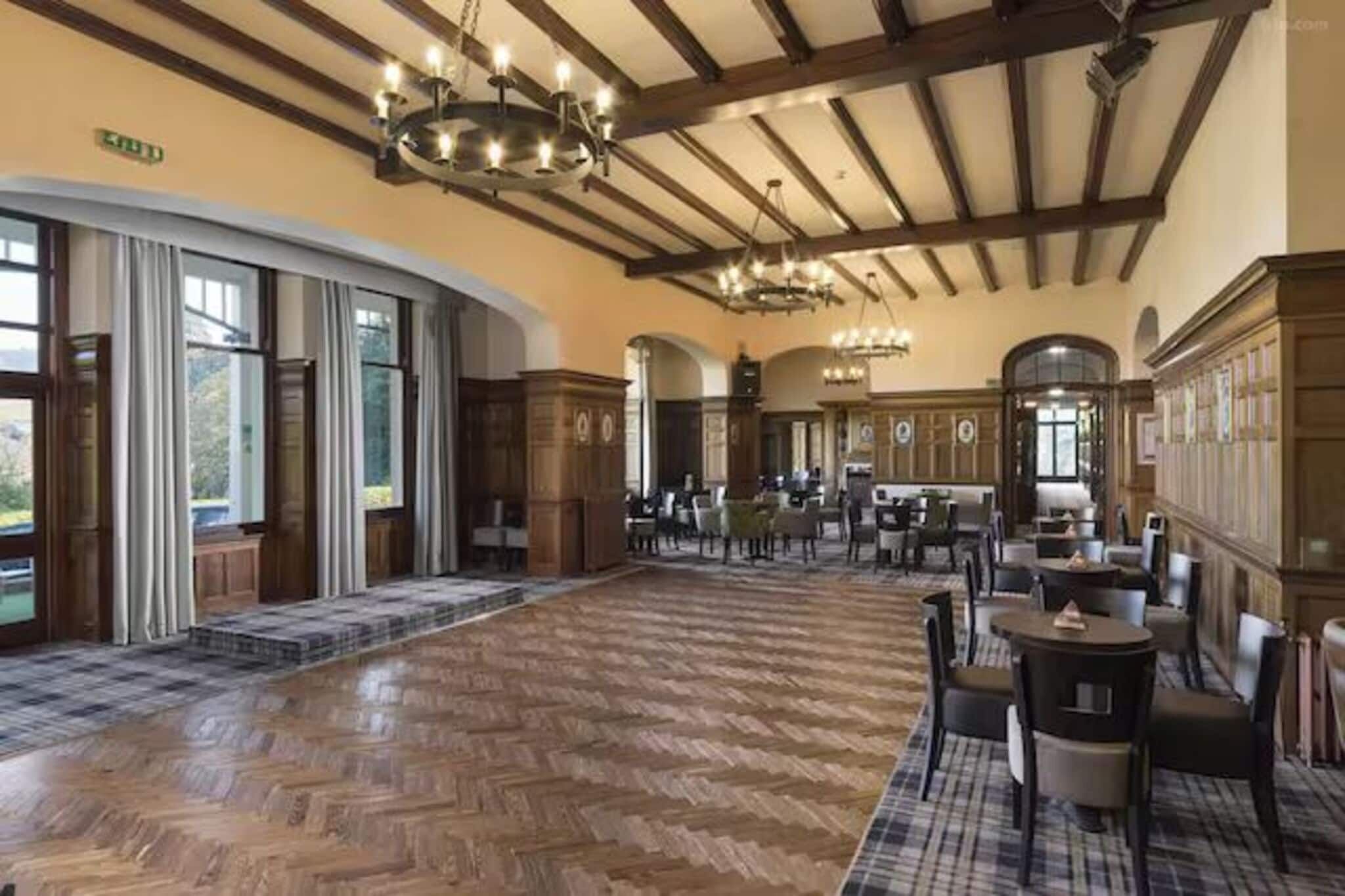 A spacious lobby with a herringbone floor, large chandeliers, and a view of the outdoors through large windows.