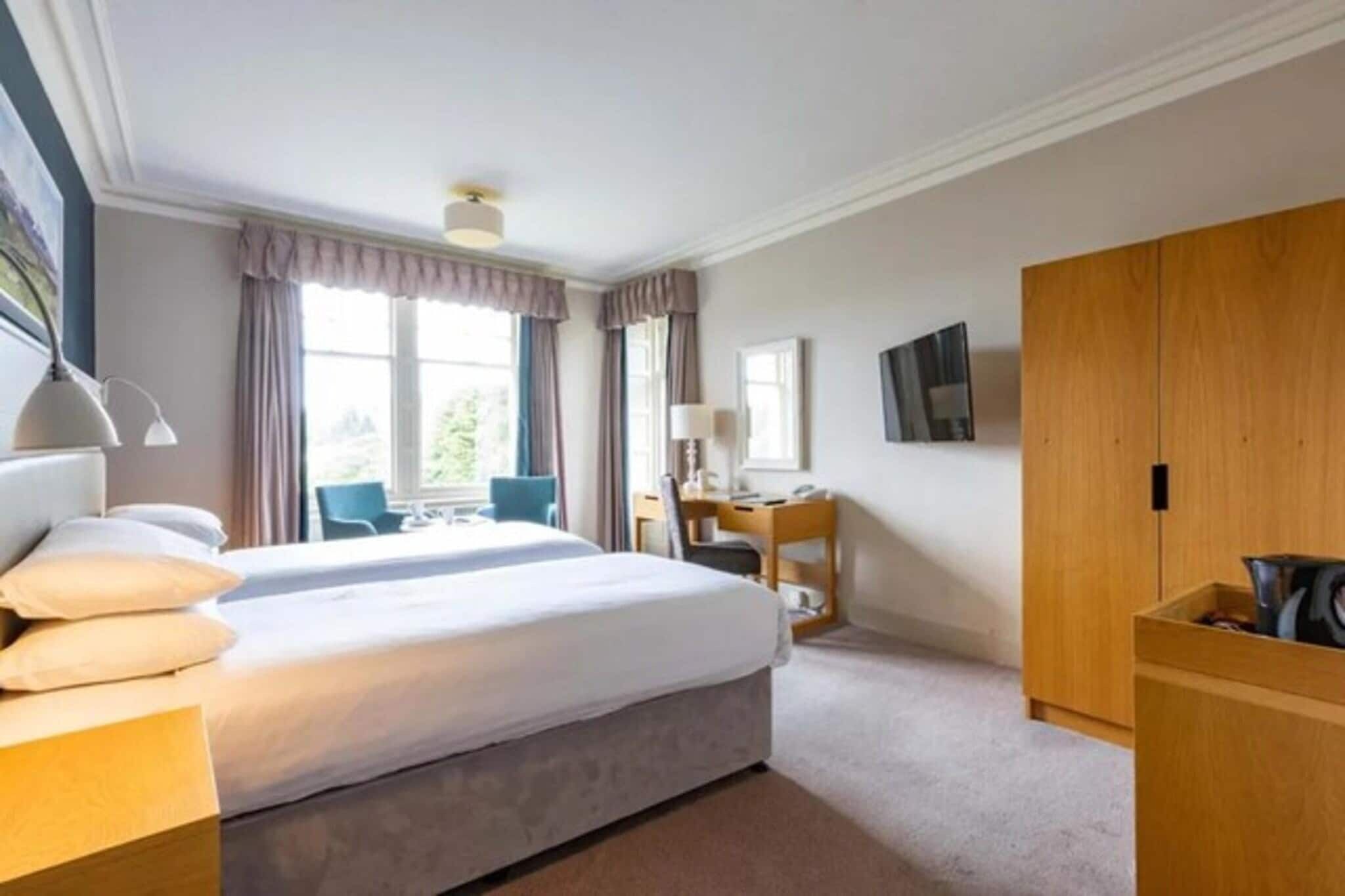 A hotel room with a bed, a desk, a chair, a wardrobe, and a window with curtains.