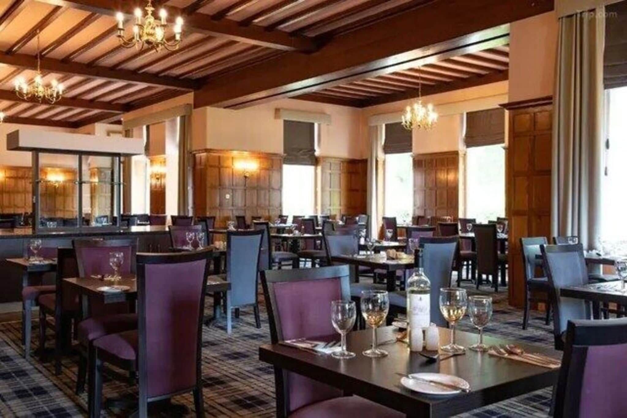 A restaurant with multiple tables and chairs, wooden ceiling beams, and chandeliers.