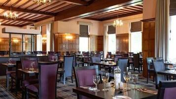 A restaurant with multiple tables and chairs, wooden ceiling beams, and chandeliers.