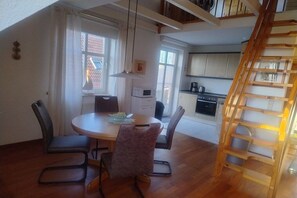 A dining area with a table and chairs, a kitchen in the background, and a wooden staircase. - Holiday apartment with 1 bedroom (Jemgum-Ditzum)