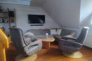 Een moderne woonkamer met een modulaire bank, twee fauteuils, een salontafel en een flatscreen televisie aan de muur.