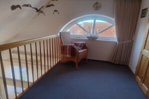 A room with a sloped ceiling, a window with a view of a building, a chair, and a wooden railing. - Holiday apartment with 1 bedroom (Jemgum-Ditzum)