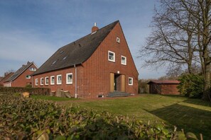 A red brick house with a sloped roof, a front door, and a small porch. - Holiday home and Lootsje (Borkum)