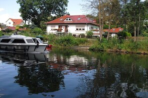 Une maison avec un toit rouge et un bateau amarré au bord d’une rivière paisible.