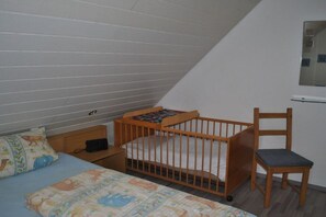 Ein Kinderzimmer mit einem Gitterbett, einem Stuhl, einem Nachttisch und einem Bett mit einem gemusterten Bettbezug.