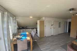 A compact kitchen with a dining area, a small refrigerator, and a door leading to another room. - Holiday apartment with 1 bedroom (Greetsiel)