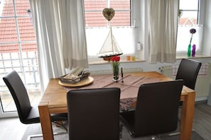 A dining area with a wooden table, black chairs, a sailboat decoration, and a vase with red flowers. - Holiday apartment with 1 bedroom (Greetsiel)