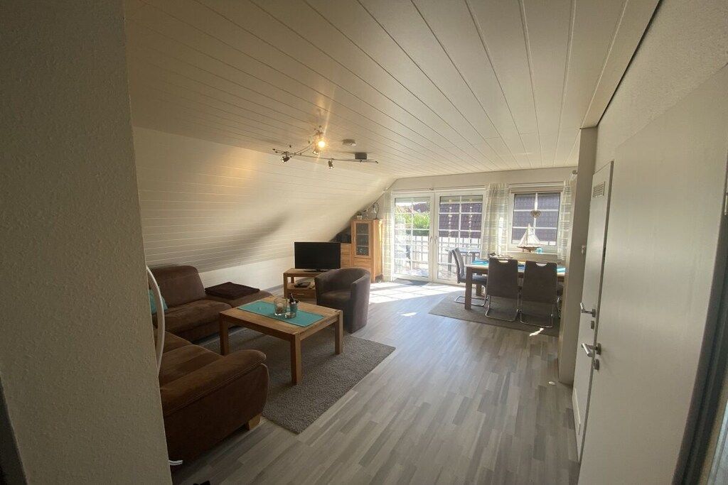 A spacious loft-style living area with a high ceiling, a dining table with chairs, a sofa, and a television.