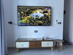 En tv som är monterad på väggen, ett vitt träskåp med lådor och en liten pall.